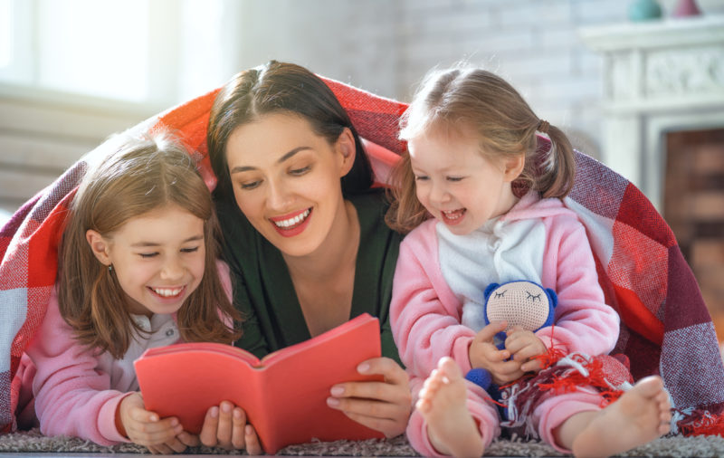 young mother reading book to children